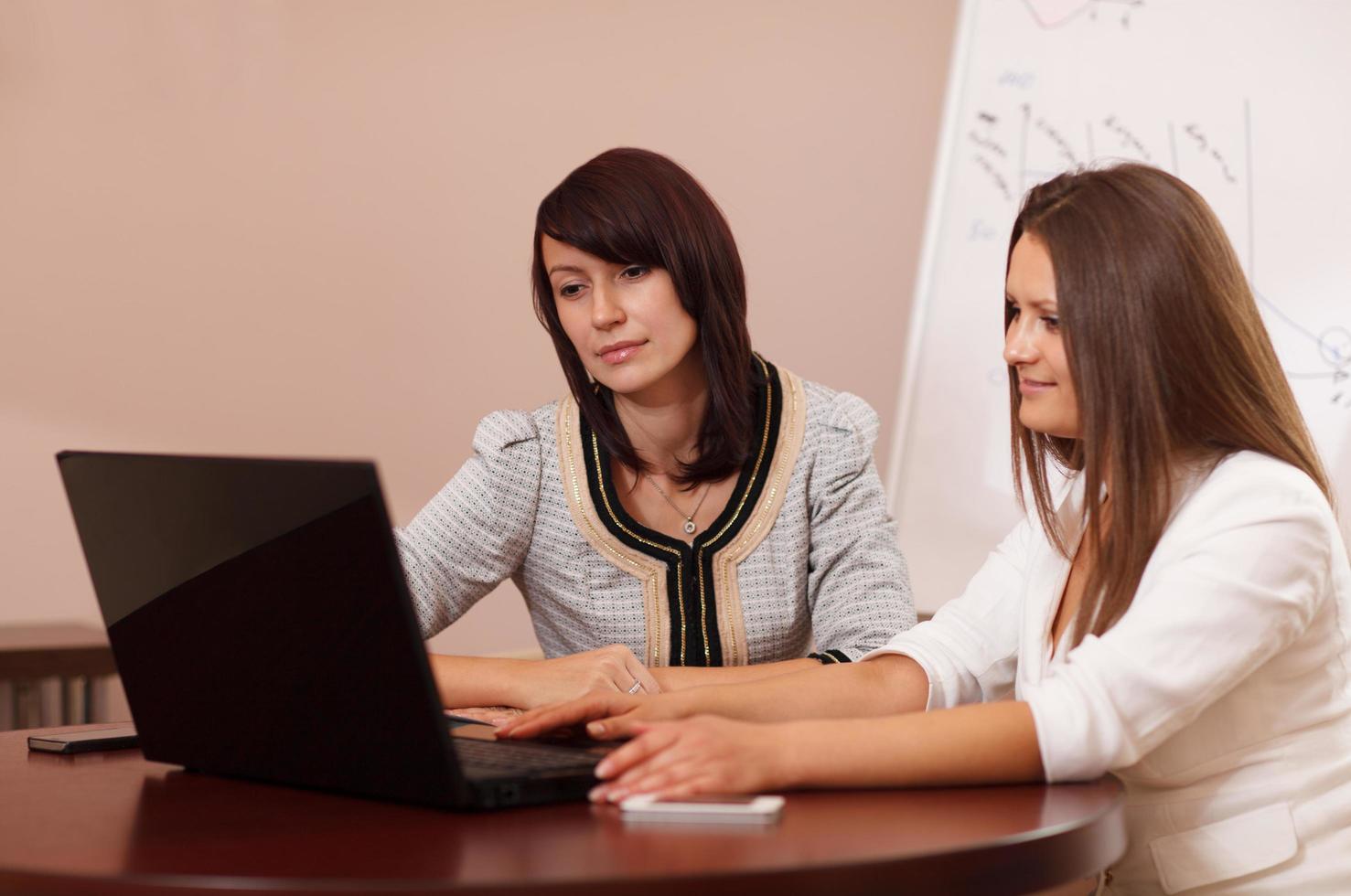 dos mujeres sentadas en una mesa con una computadora portátil foto