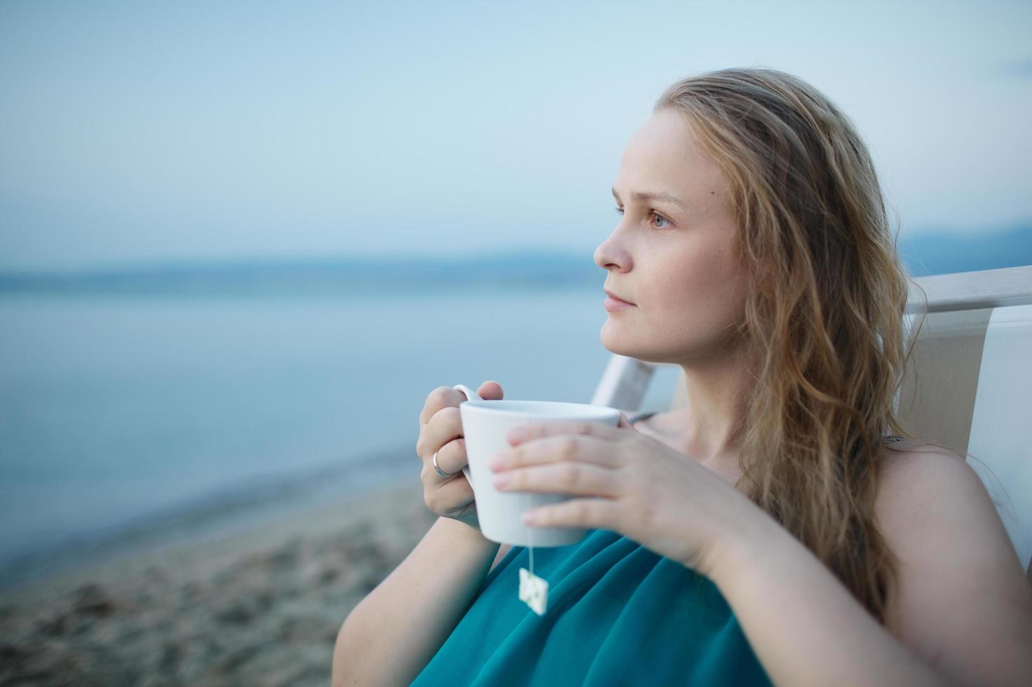 mujer disfrutando de una taza de té en la playa foto