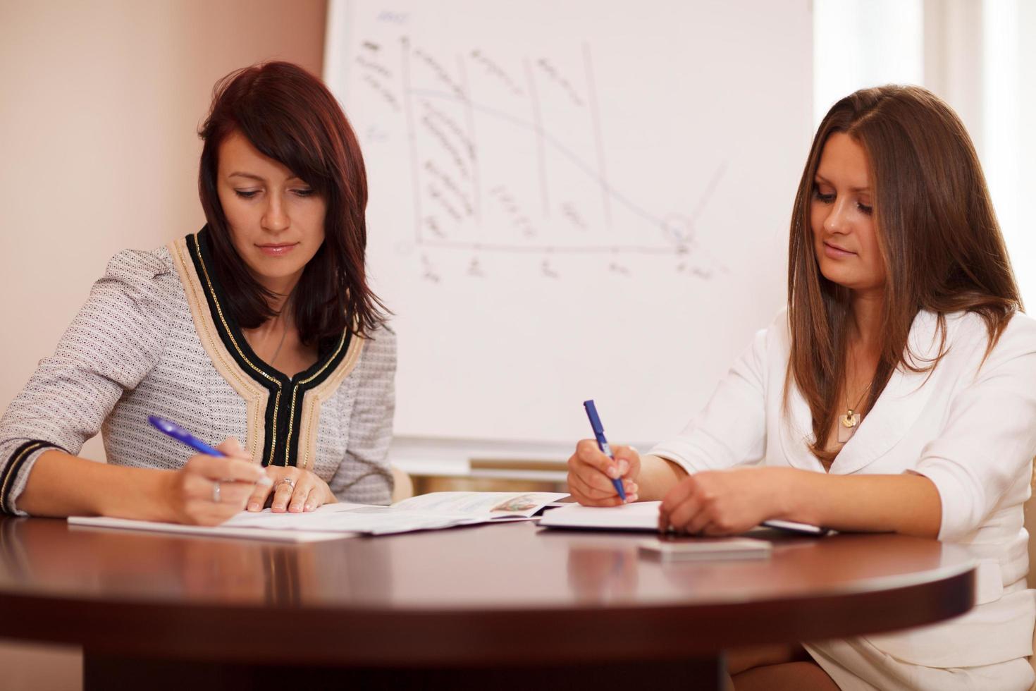 Two women taking notes at a business presentation photo