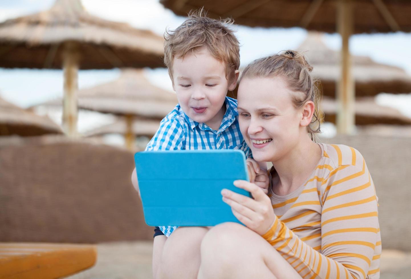 Happy mother and son at a beach resort with a tablet photo