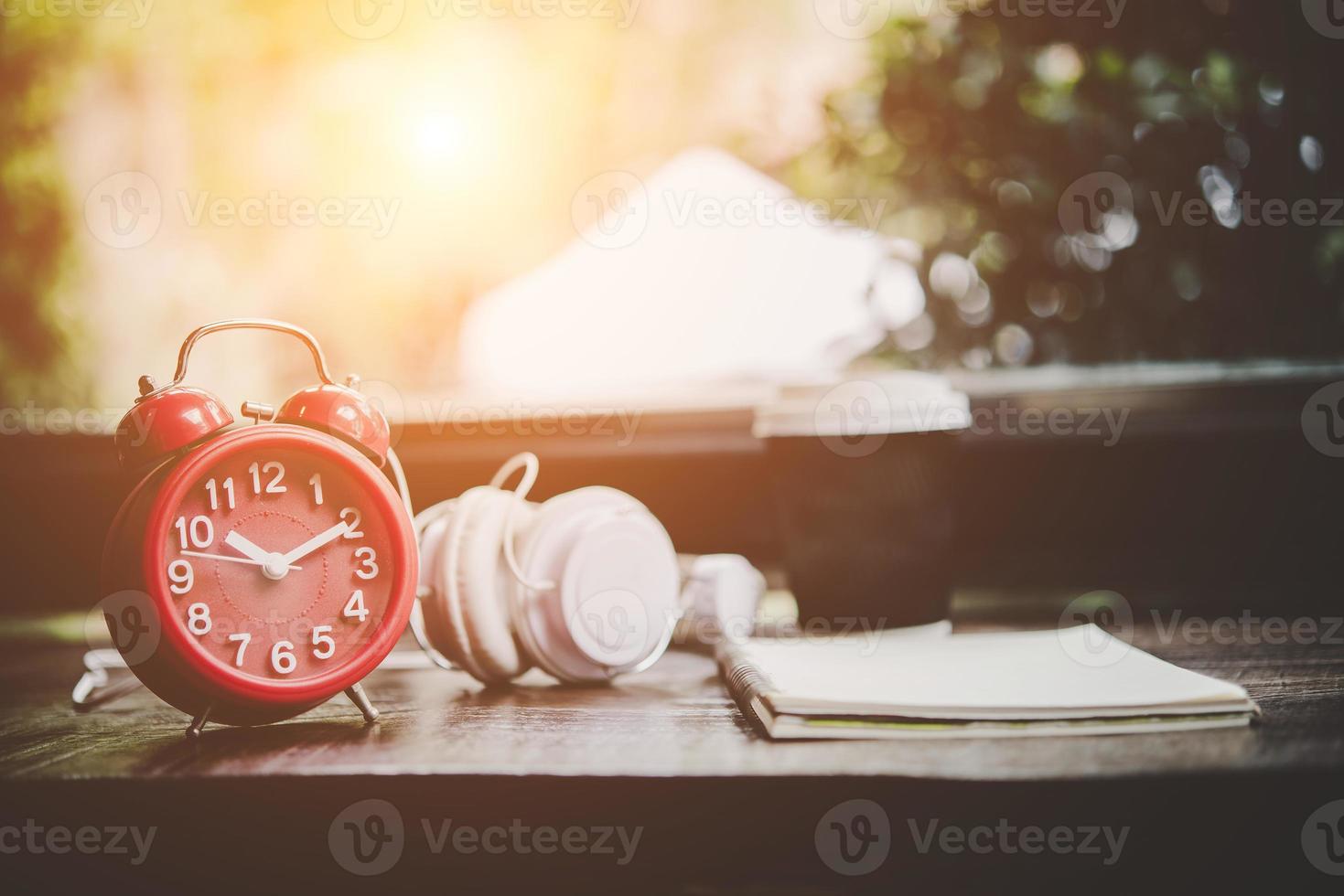 Taza de café, cuaderno y despertador rojo con auriculares en una mesa de madera foto