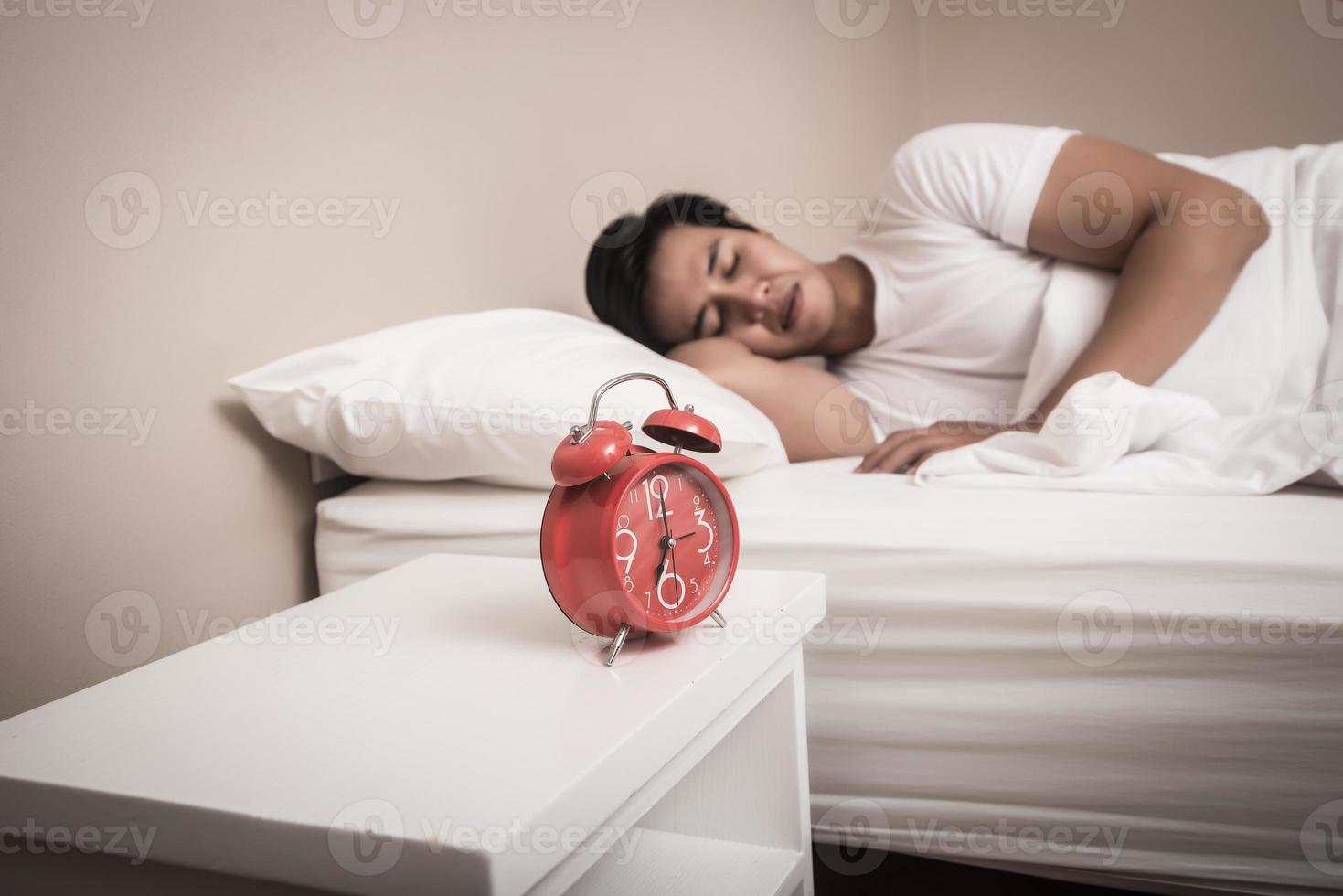 El hombre duerme en la cama con despertador rojo foto