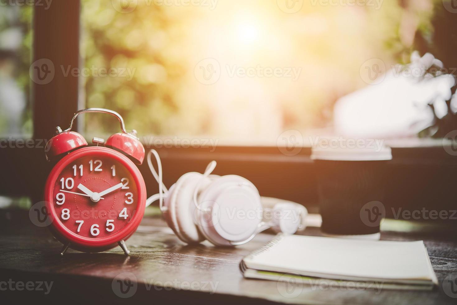 Taza de café, cuaderno y despertador rojo con auriculares en una mesa de madera foto