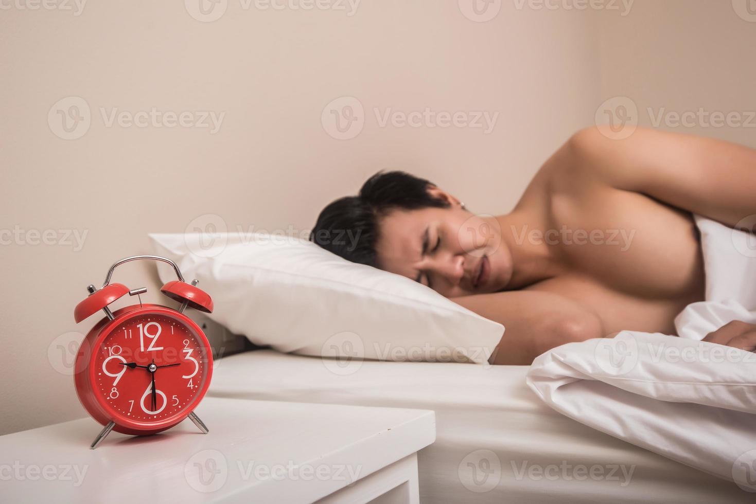 El hombre duerme en la cama con despertador rojo foto