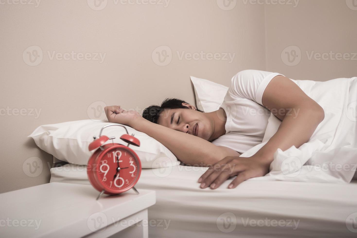 El hombre duerme en la cama con despertador rojo foto