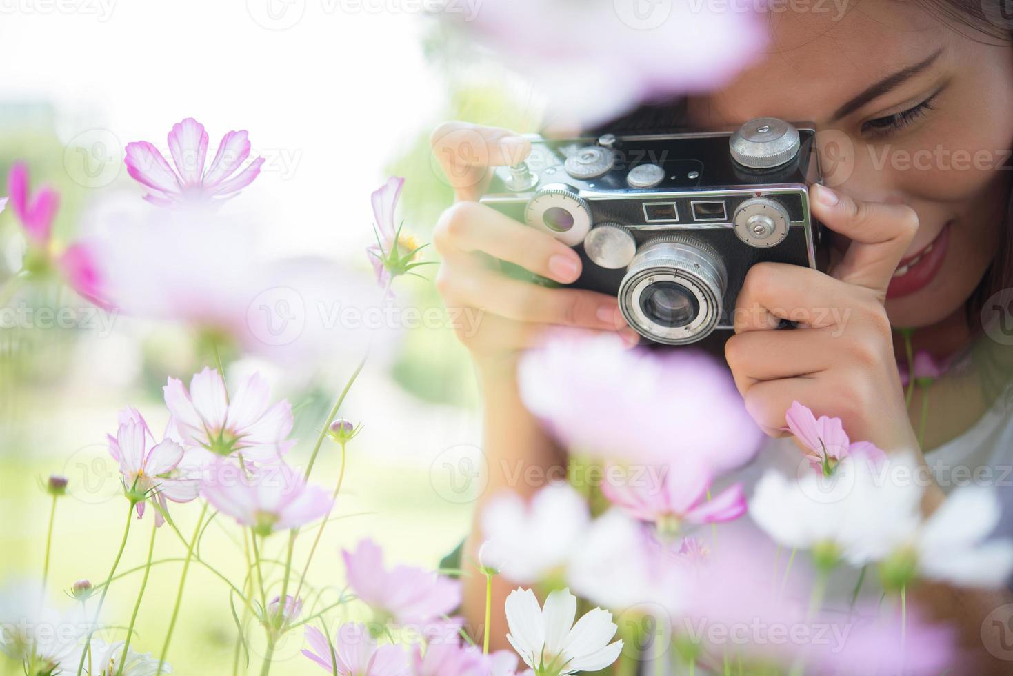 Chica hipster con enfoque de cámara vintage disparando flores en un jardín. foto