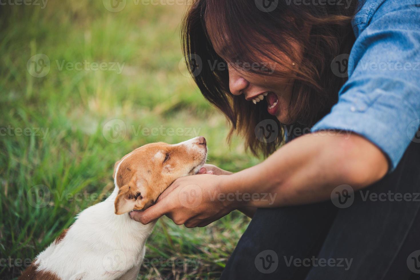 Feliz chica hipster alegre jugando con su perro en el parque durante la puesta de sol foto