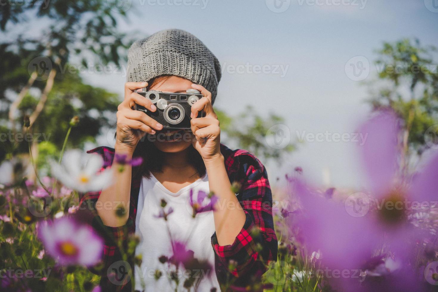 Chica hipster con enfoque de cámara vintage disparando flores en un jardín. foto