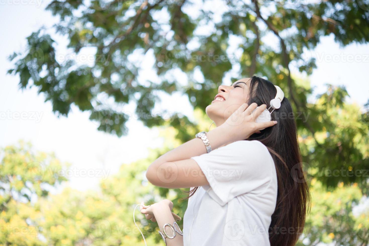 Retrato de una niña sonriente con auriculares escuchando música en la naturaleza foto