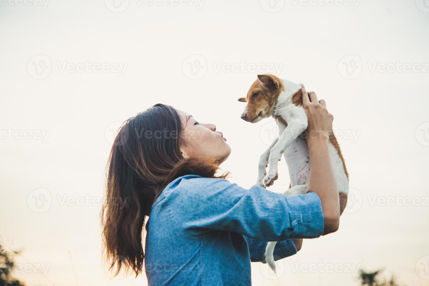 Feliz chica hipster alegre jugando con su perro en el parque durante la puesta de sol foto