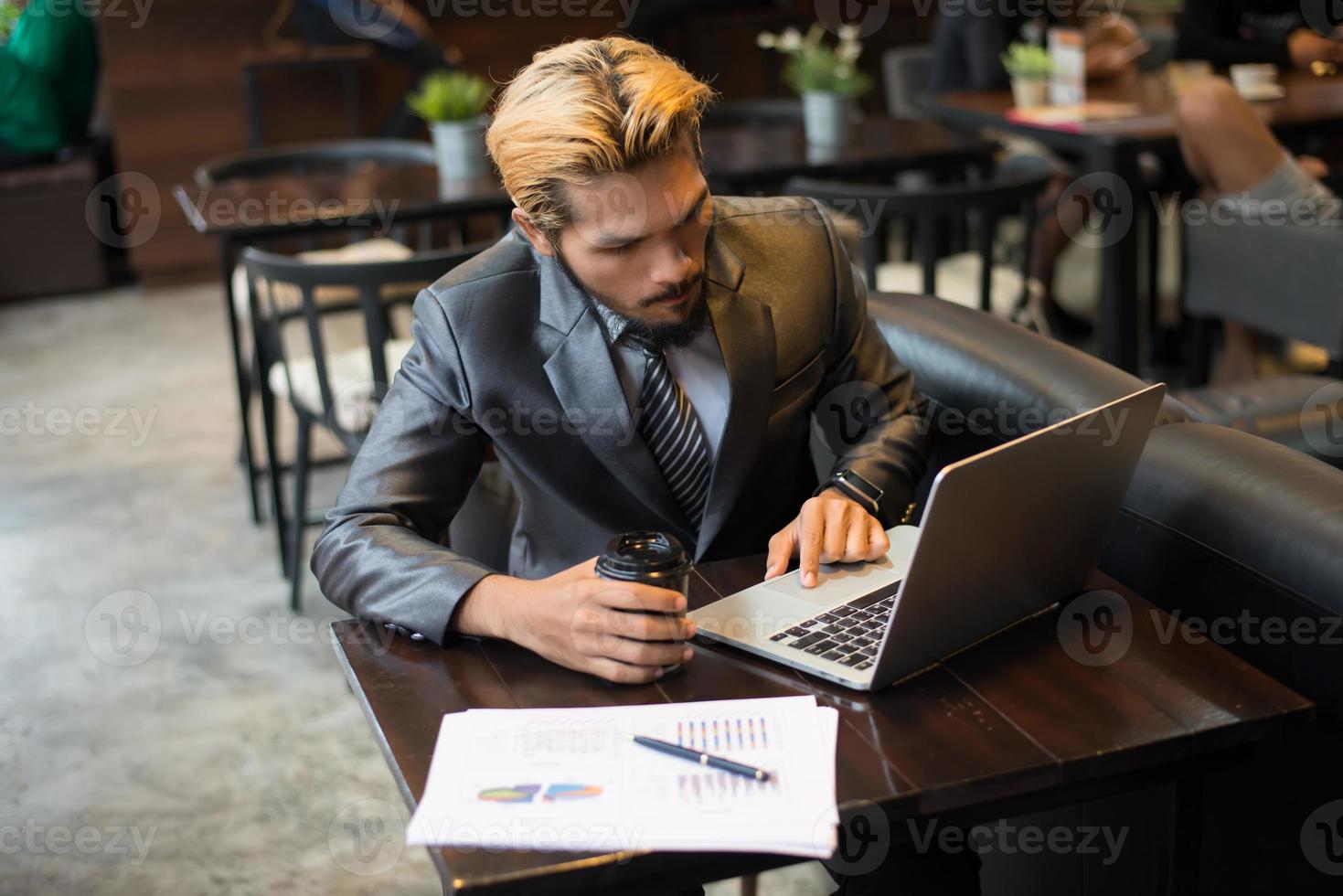 Young businessman holding cup of coffee while working on laptop computer in coffee shop photo