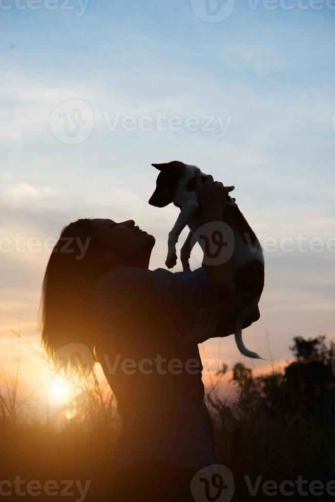 Silhouette of a woman holding small dog at sunset field photo