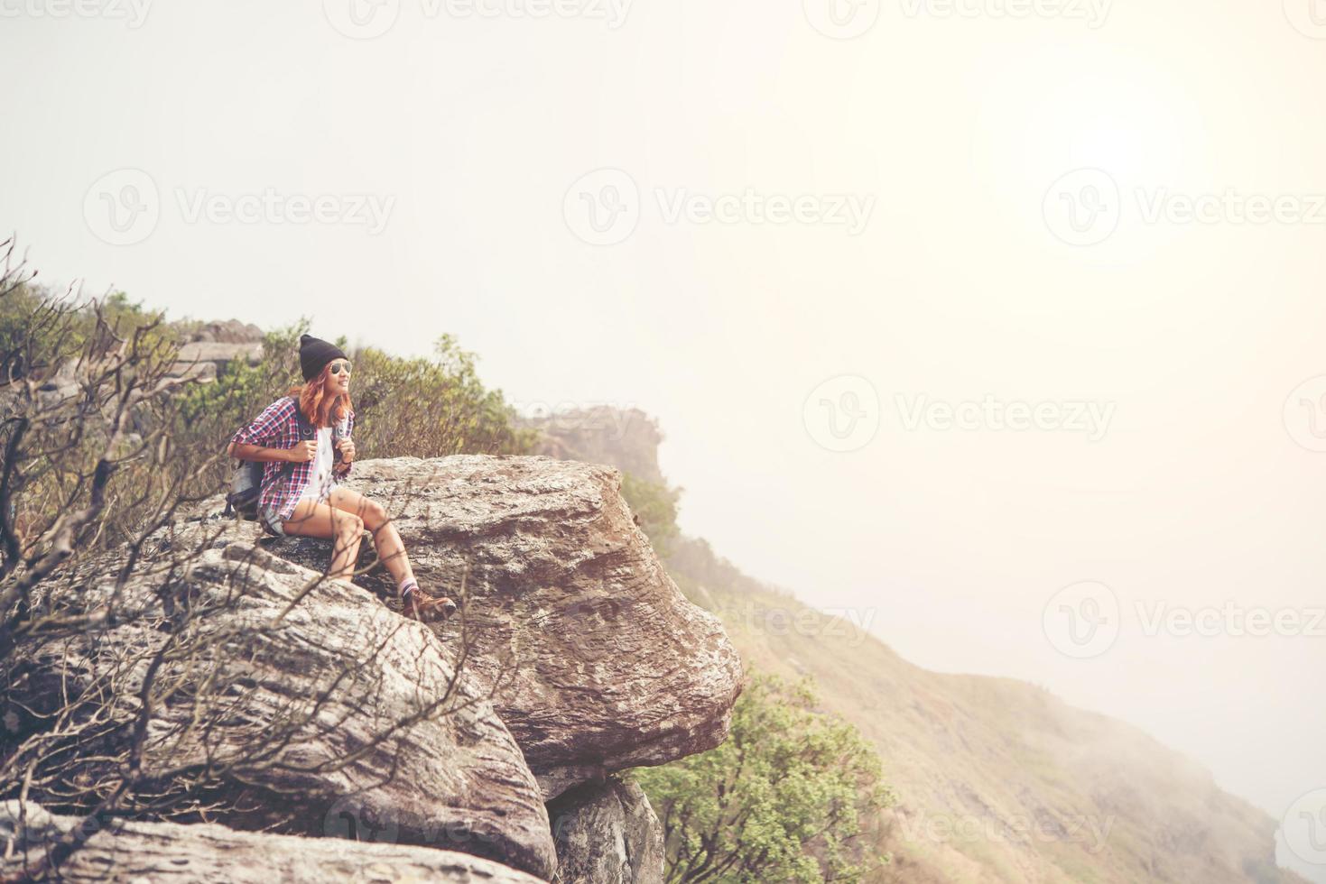 Young hiker with backpack sits on the edge of the cliff photo