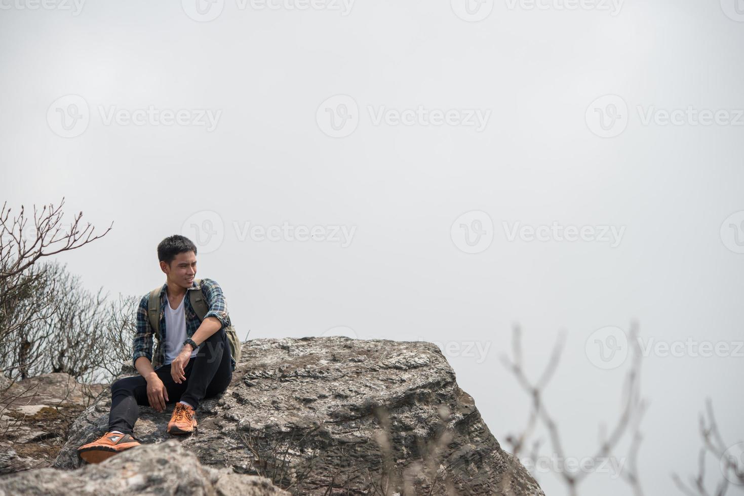 Young hipster hiker with backpack sitting on top of the mountain photo