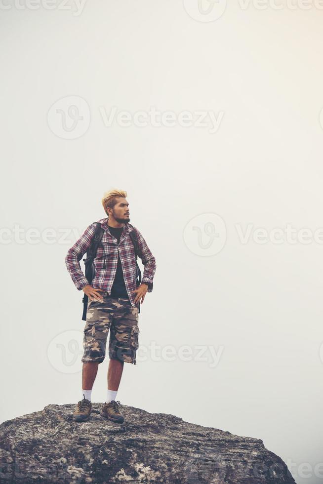 Young hipster hiker with backpack sitting on top of the mountain photo