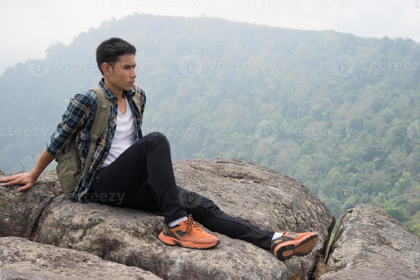 Excursionista joven inconformista con mochila sentado en la cima de la montaña foto