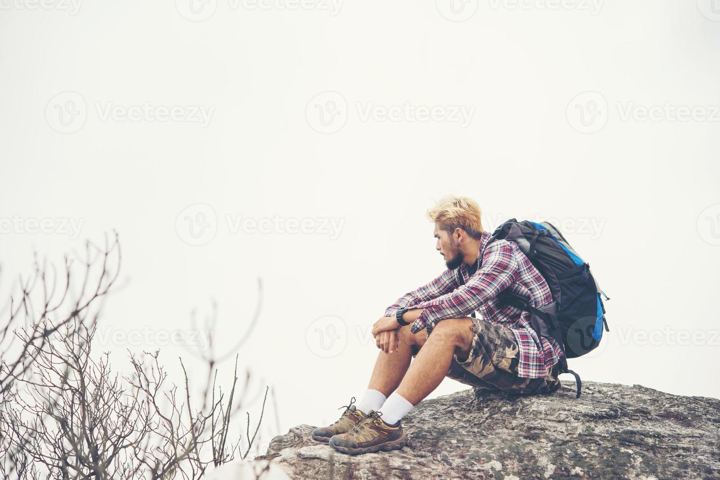 Young hipster hiker with backpack sitting on top of the mountain photo