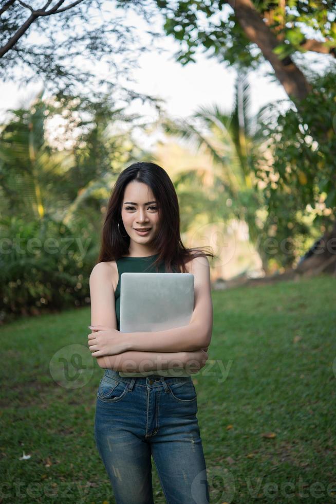 Hermosa joven sosteniendo una computadora portátil mientras va a relajarse en un parque foto