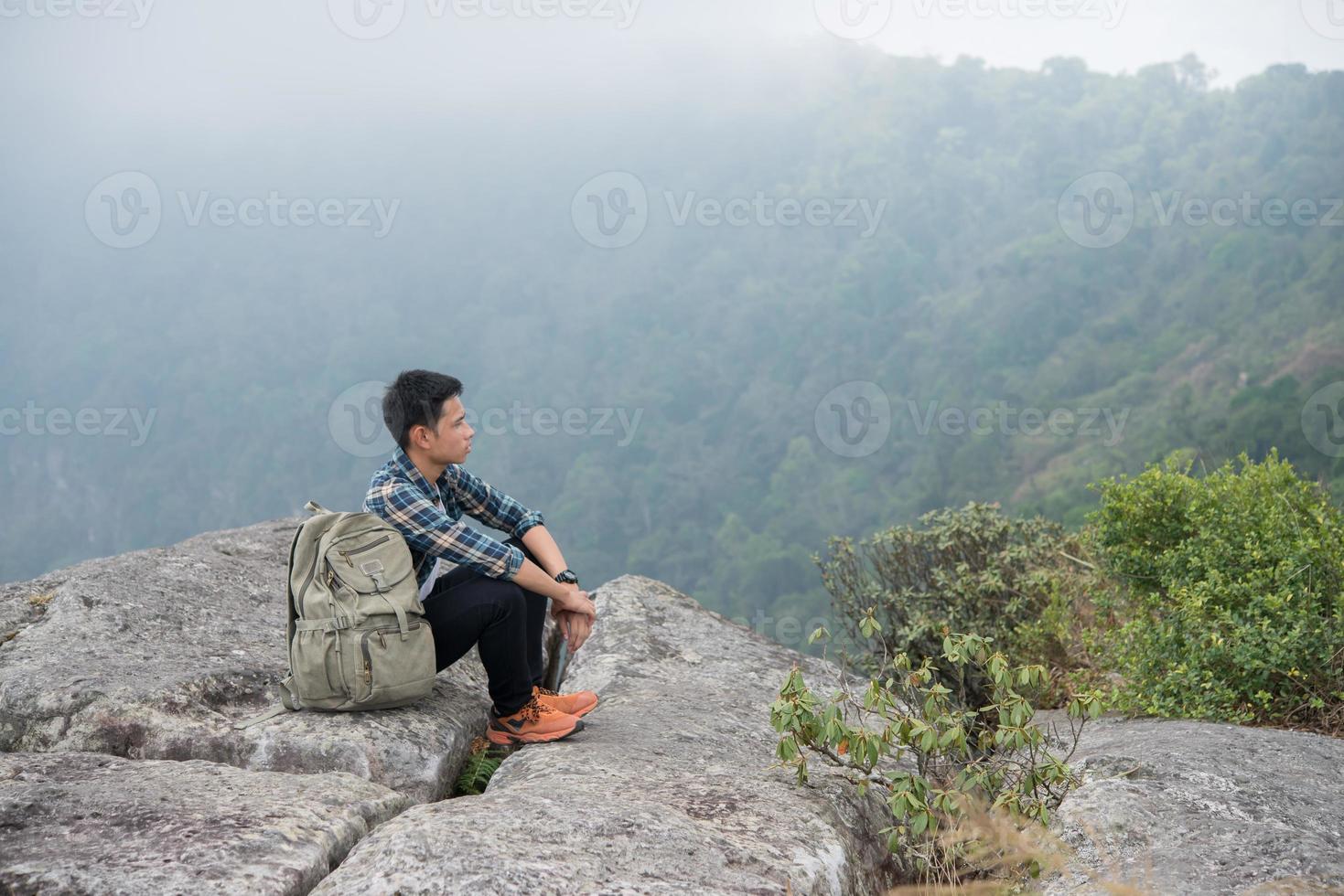 Young hipster hiker with backpack sitting on top of the mountain photo