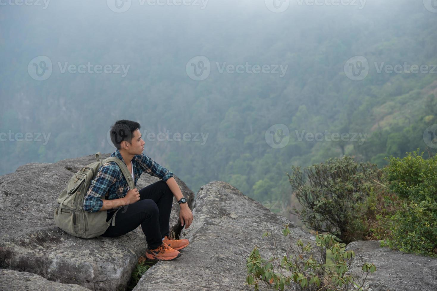 Excursionista joven inconformista con mochila sentado en la cima de la montaña foto