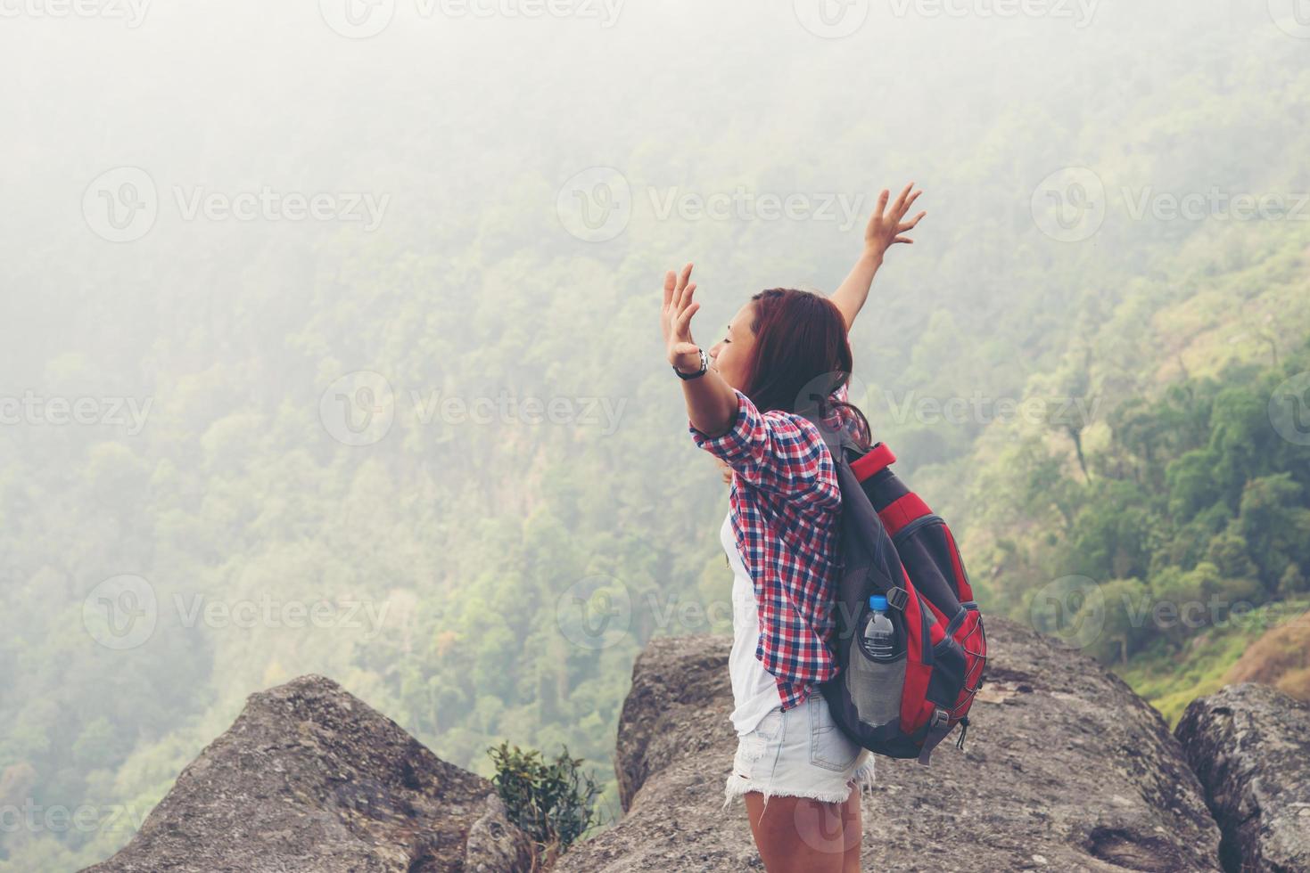 Caminante con mochila de pie en la cima de una montaña con las manos levantadas foto