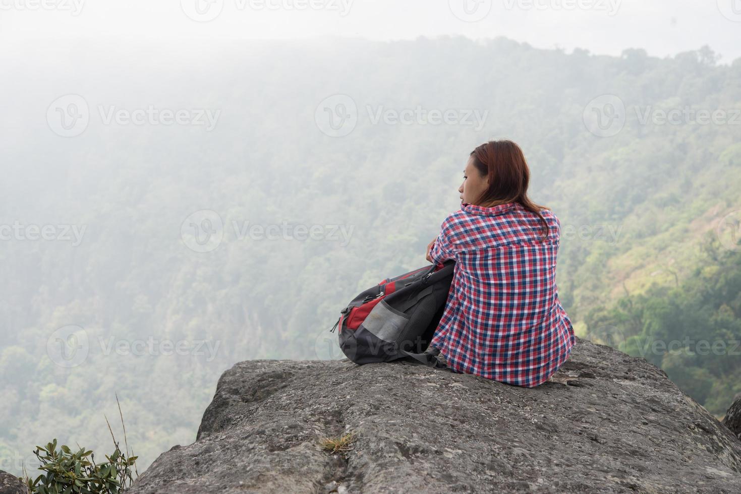 Young hiker with backpack sits on the edge of the cliff photo