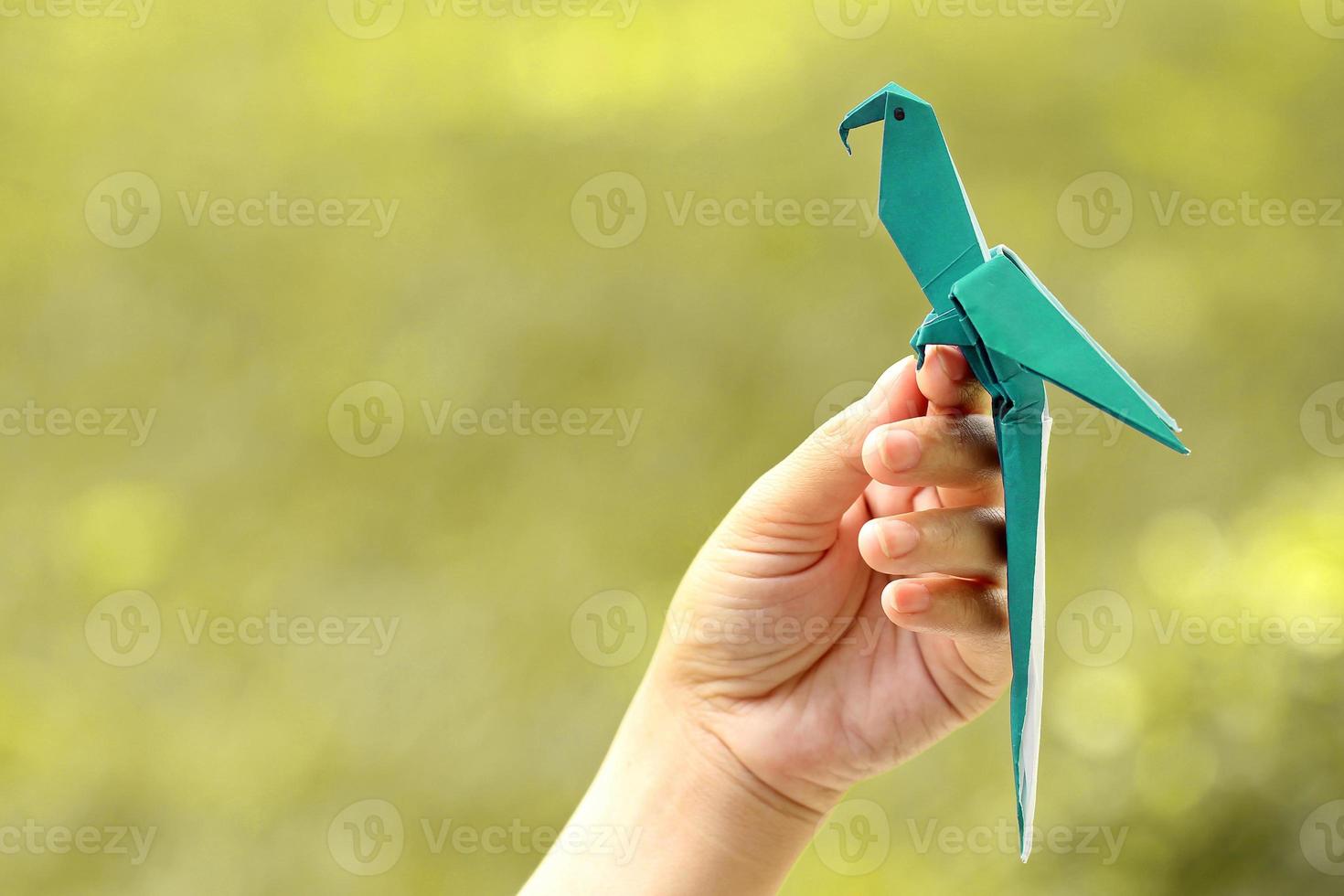 Mano que sostiene el pájaro de origami azul con fondo de naturaleza borrosa foto
