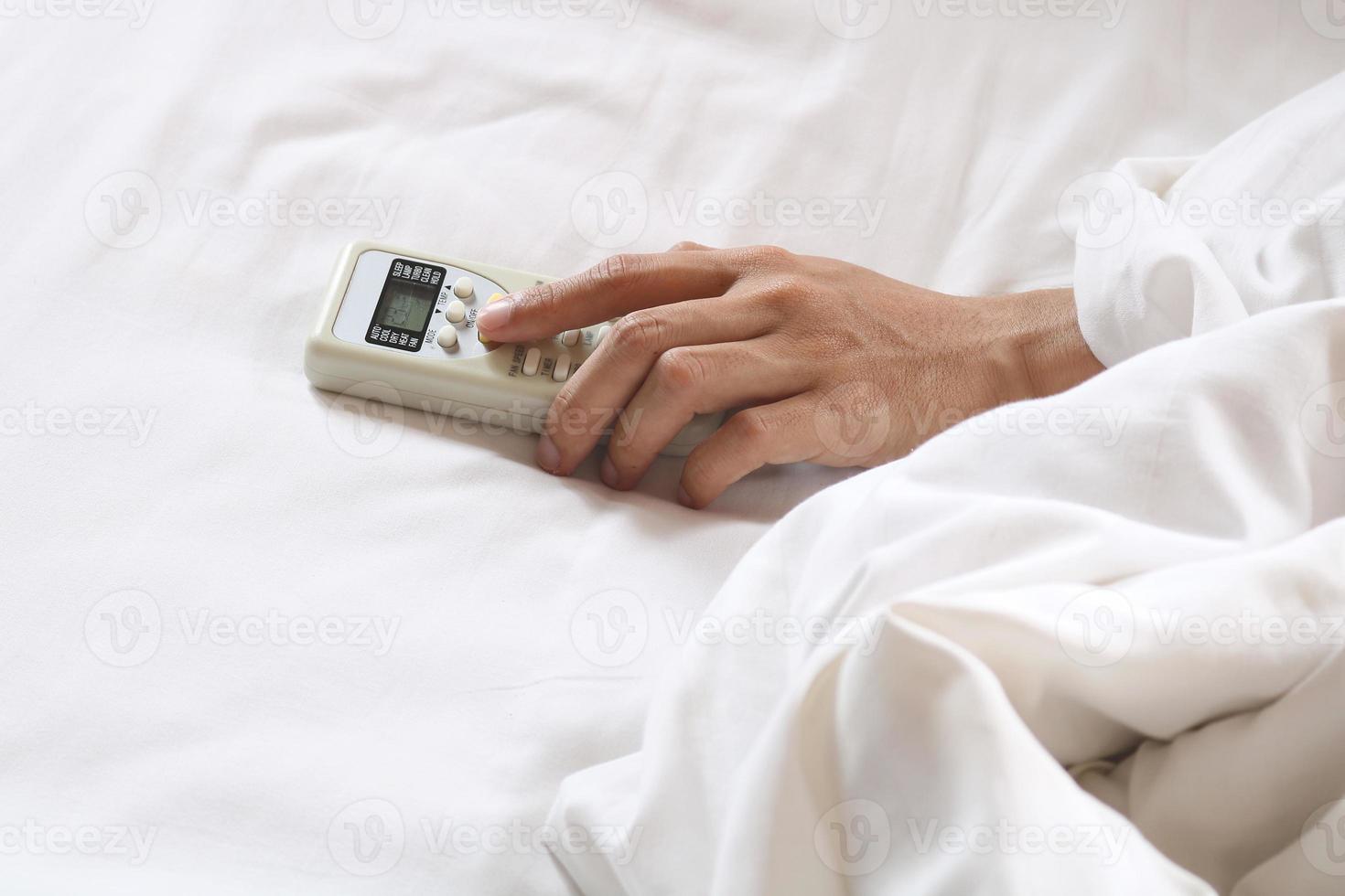 Mano sujetando el control remoto del aire acondicionado en la cama foto