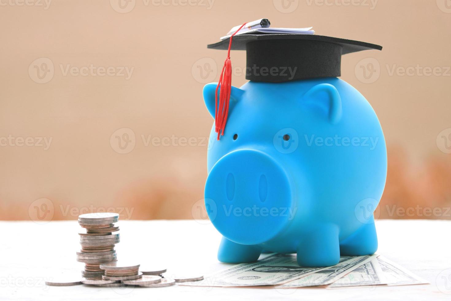 Coins stacks next to blue piggy bank wearing a mortarboard photo