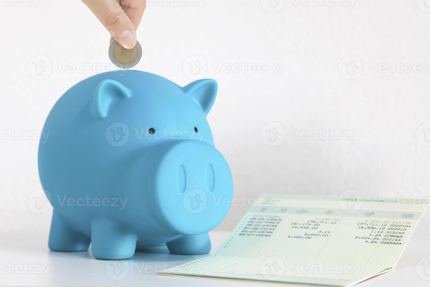 Hand inserting coin into blue piggy bank photo