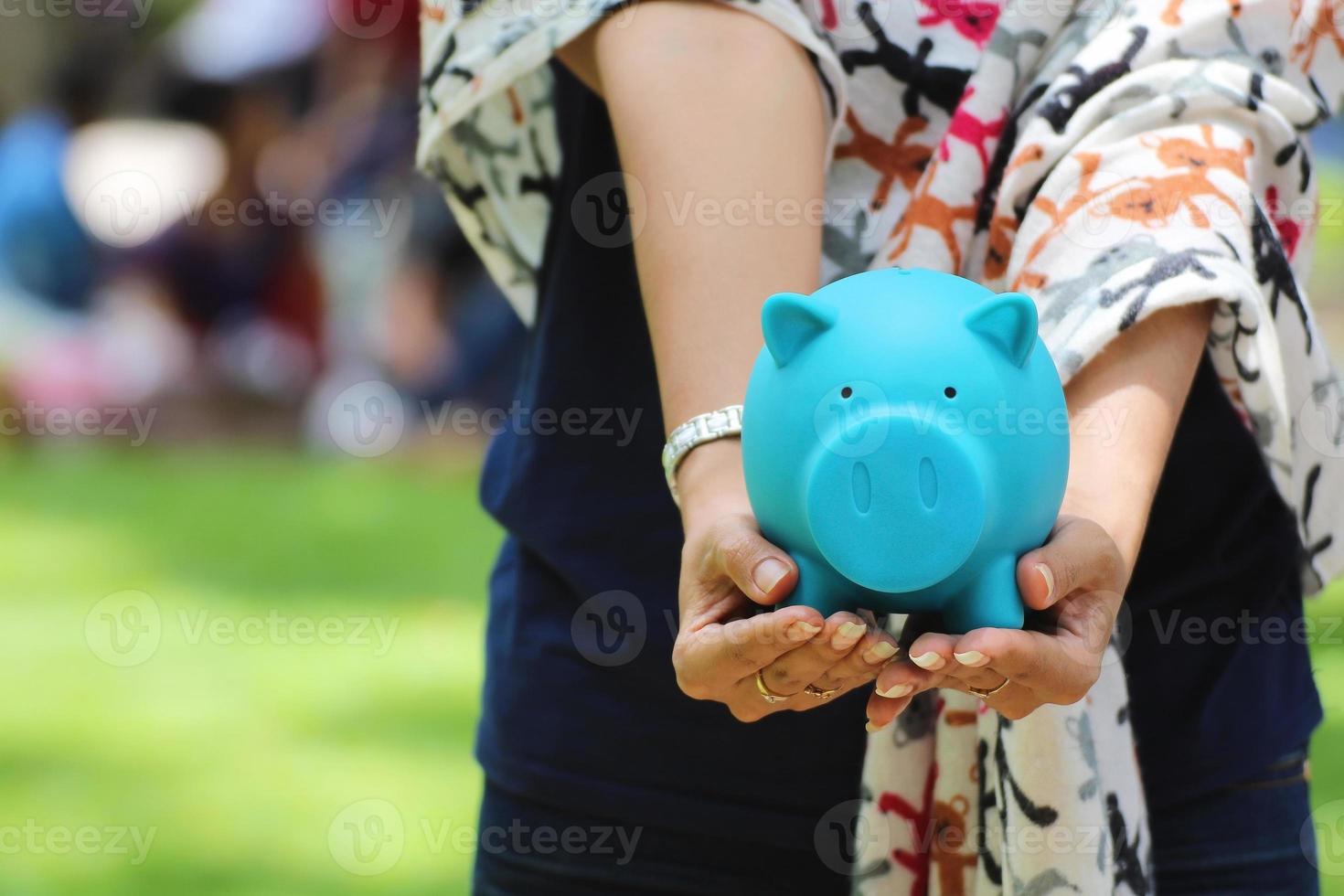 Outstretched arms and hands holding blue piggy bank with outdoor background photo