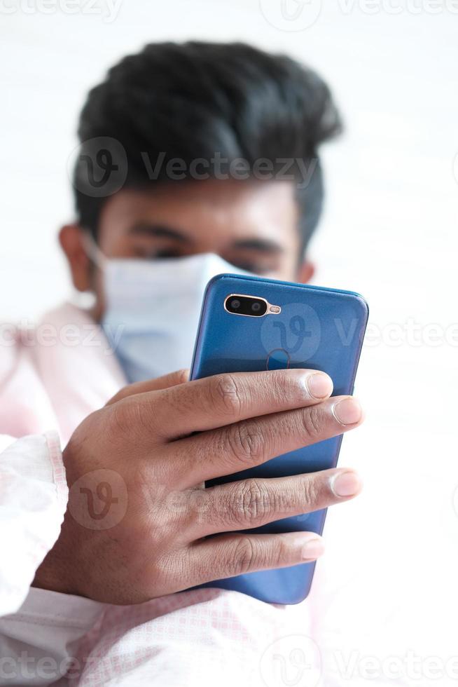 Sick man in surgical face mask using smartphone, selective focus photo