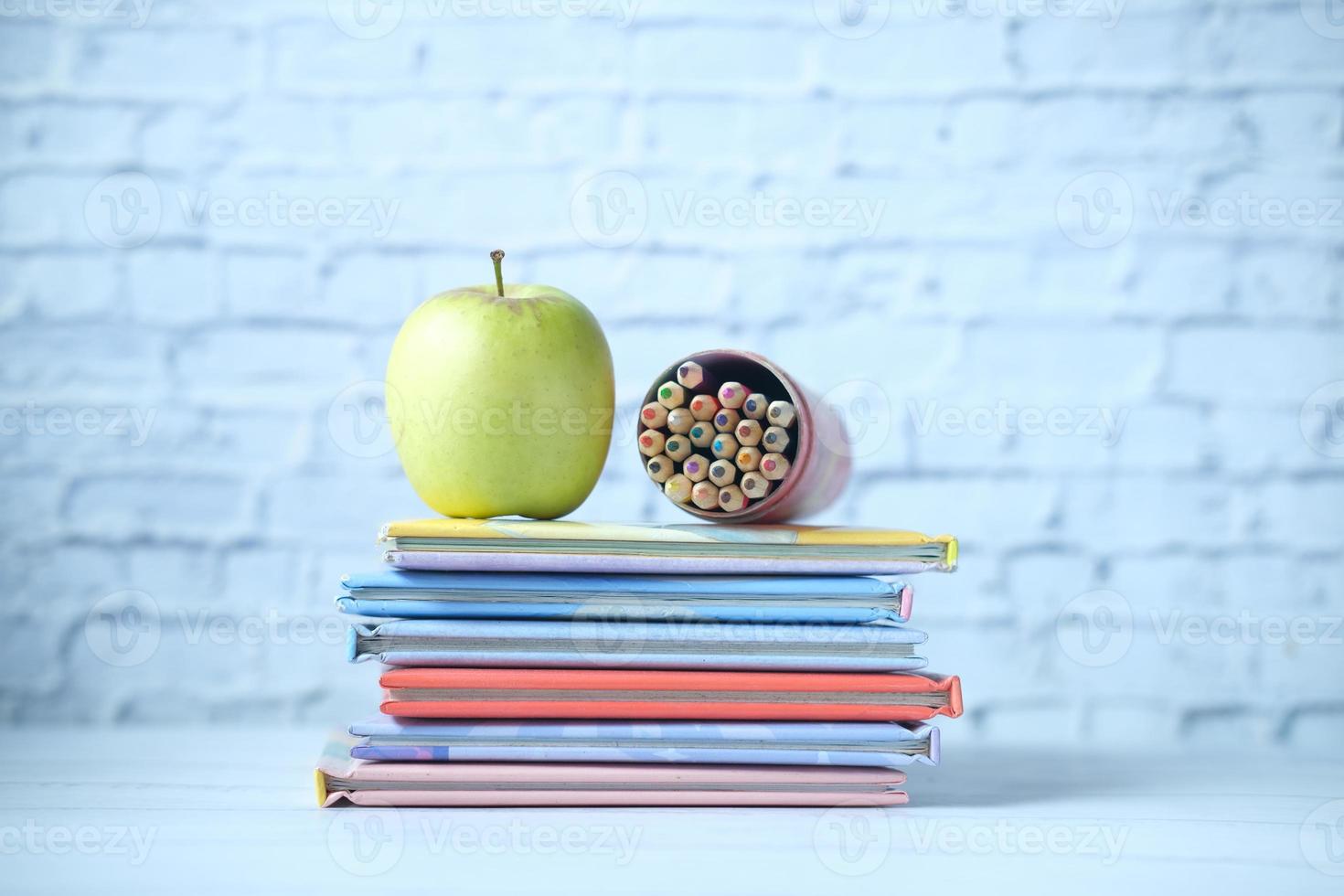 libros coloridos, una manzana y un lápiz de color en la mesa foto