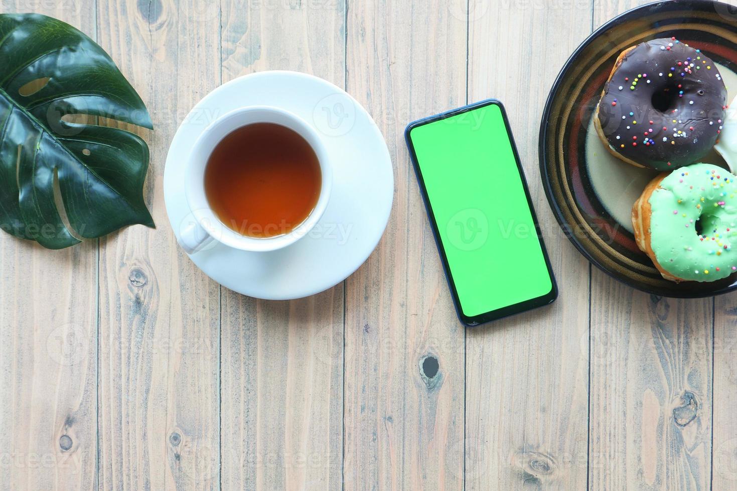 Vista superior del teléfono inteligente con pantalla vacía, té y donas en la mesa foto