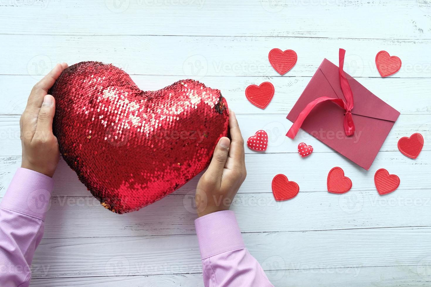 A hand holding a red heart made of sequins on table, top view photo