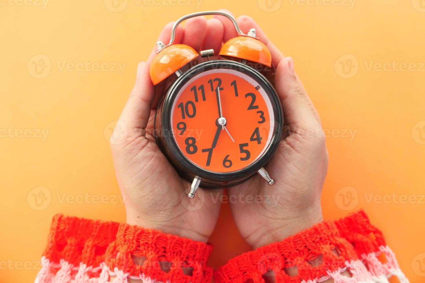 Mano de mujer sosteniendo un despertador sobre fondo naranja foto