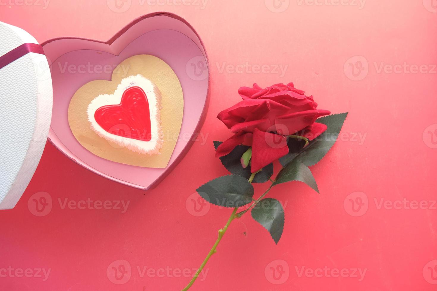 Top view of heart shape cake, gift box, and rose flower on red background photo