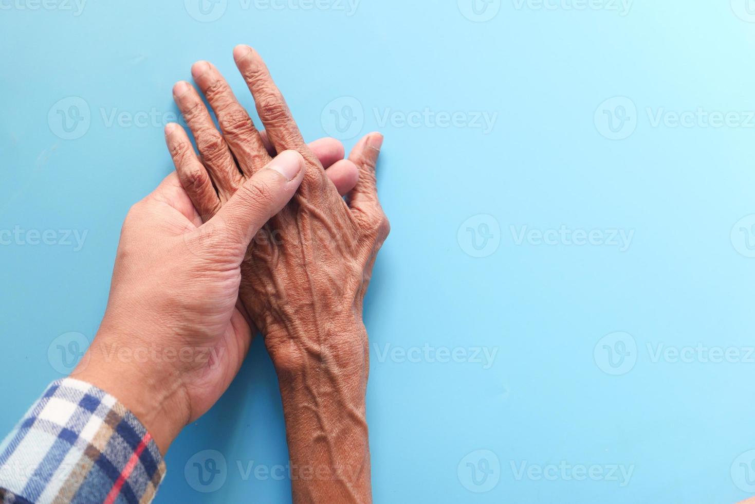 Hombre sujetando la mano de una mujer mayor sobre fondo azul. foto