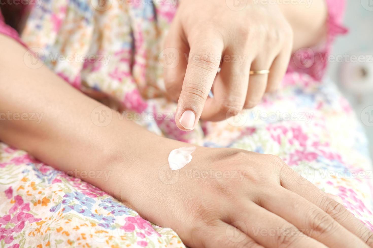 Woman applying beauty cream onto skin at home, top view photo