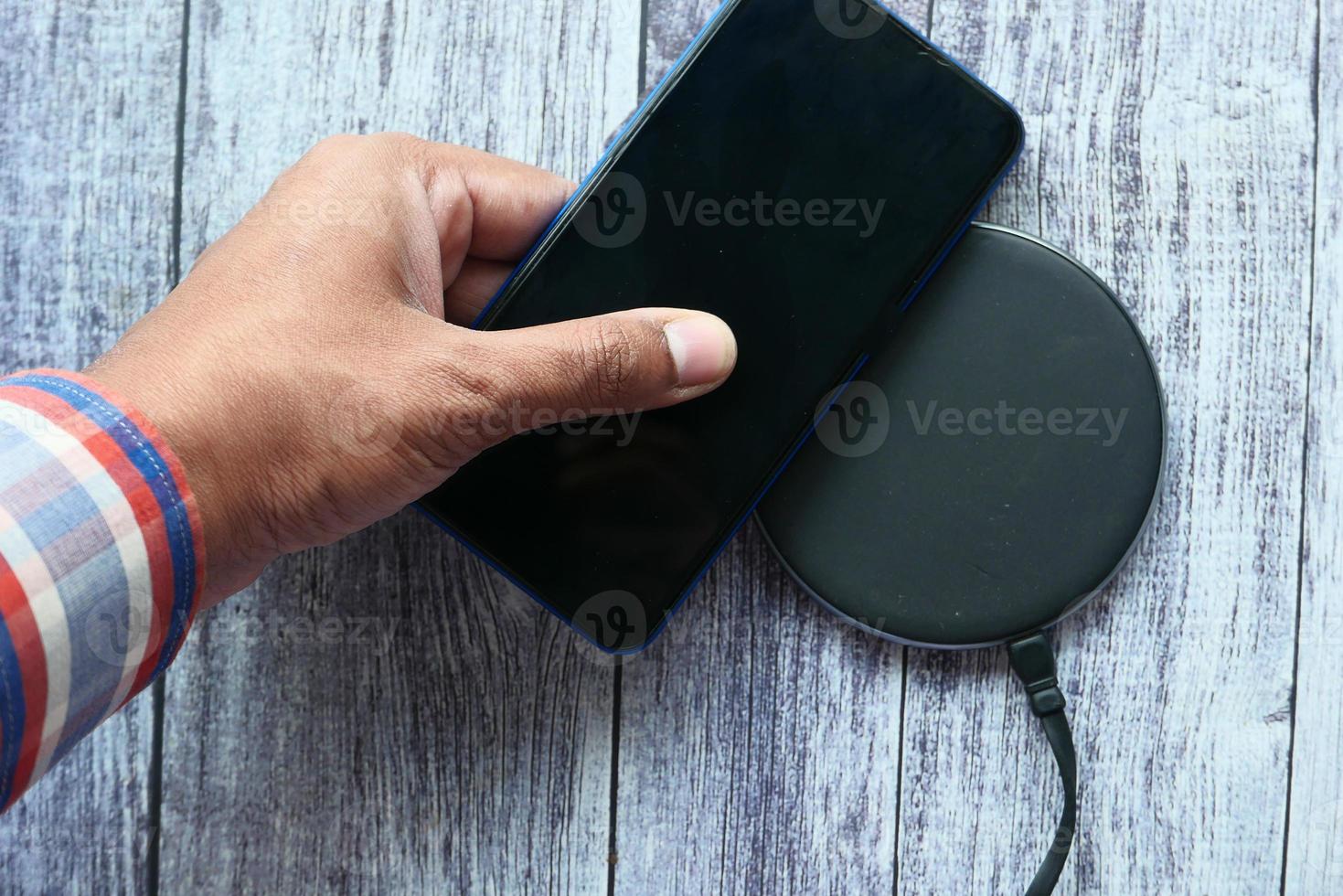 Man's hand charging a smartphone using wireless charging pad, top view photo