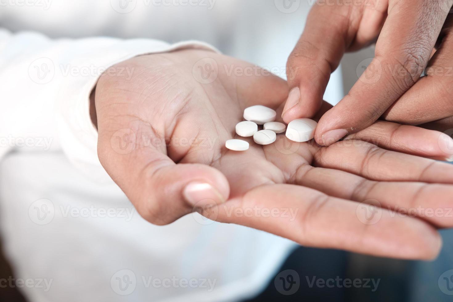 La mano del hombre con la medicina derramada fuera del contenedor de pastillas foto