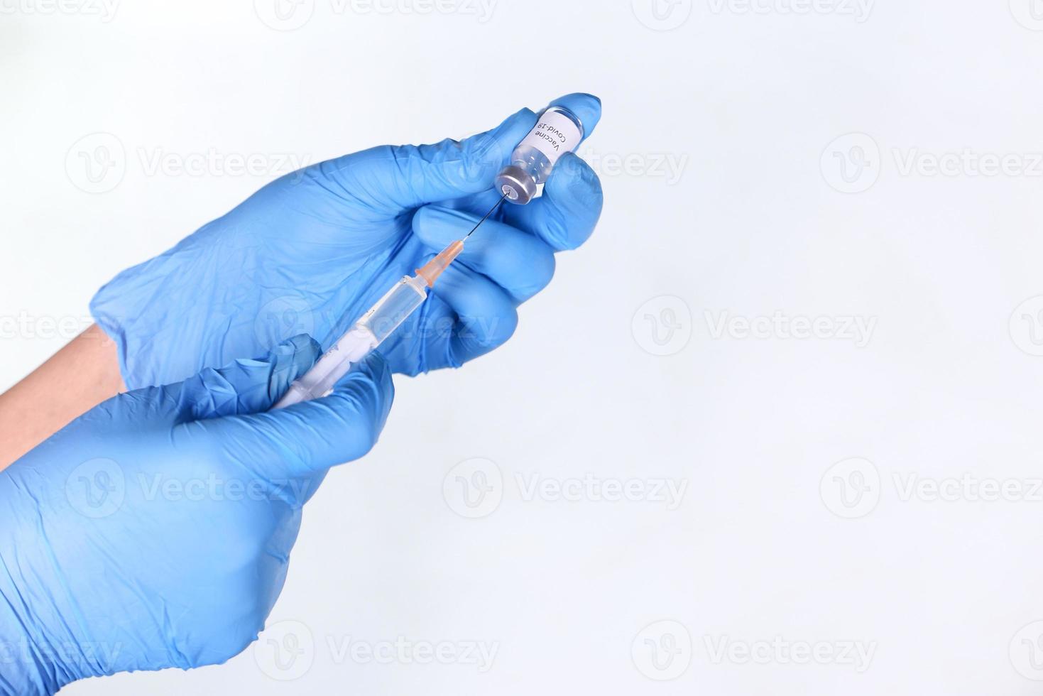 Mano en guantes de látex azul jeringa de llenado con medicamento aislado sobre fondo blanco. foto