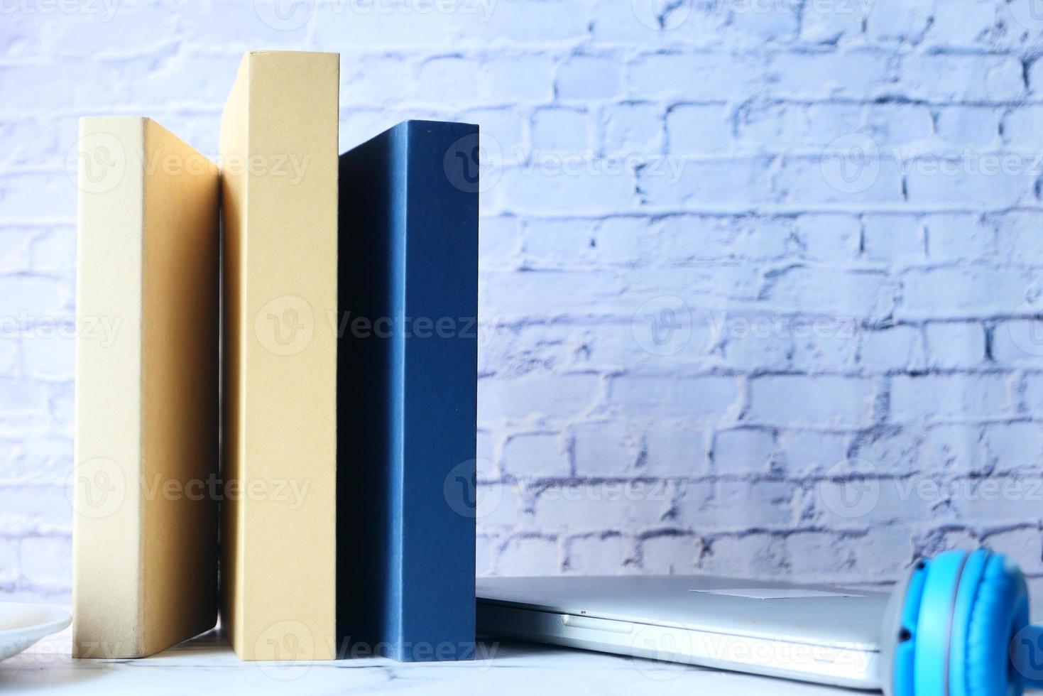 Stack of books, laptop and clock on table, close-up photo