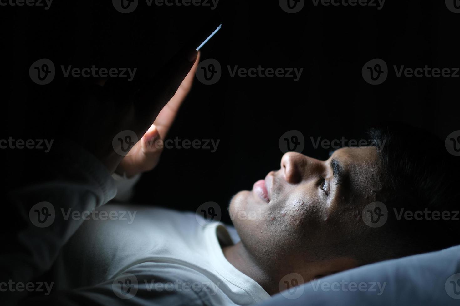 Young man on bed looking at smartphone at night photo