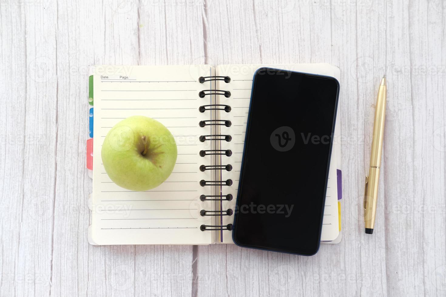 Top view of smartphone , apple and notepad on table photo