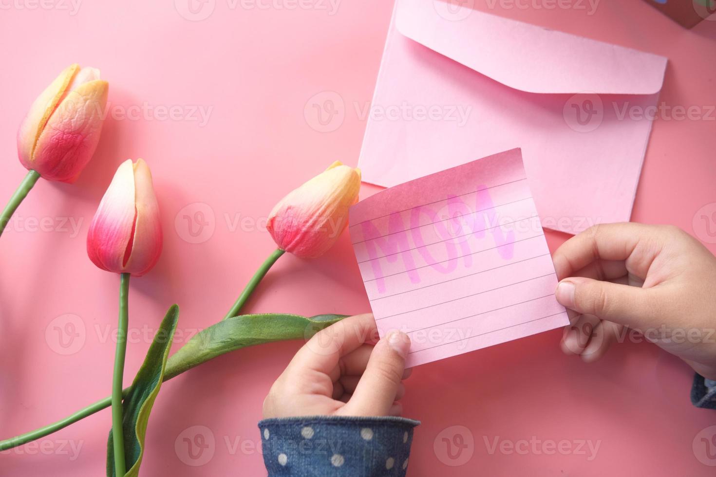 vista superior de la mano del niño que sostiene el regalo del día de la madre y una flor en rosa foto