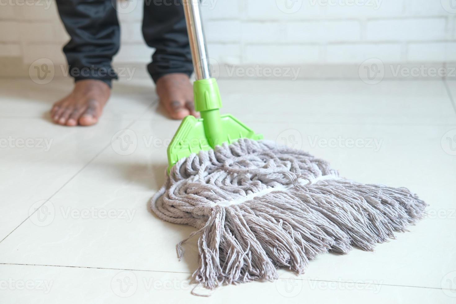 Barefoot person cleaning tile floor with mop photo