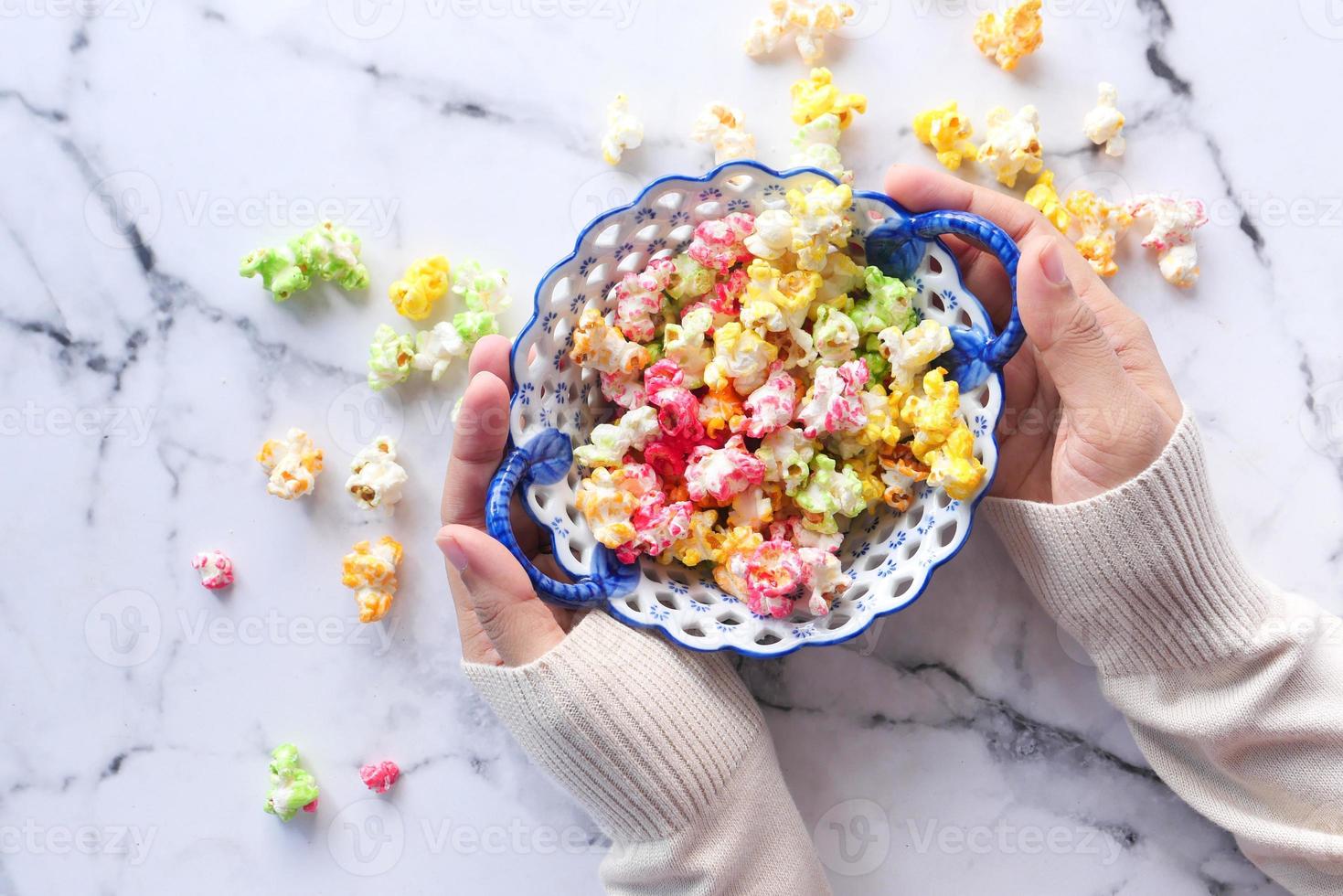 Vista superior de las manos de la mujer sosteniendo un tazón de palomitas de maíz de colores foto