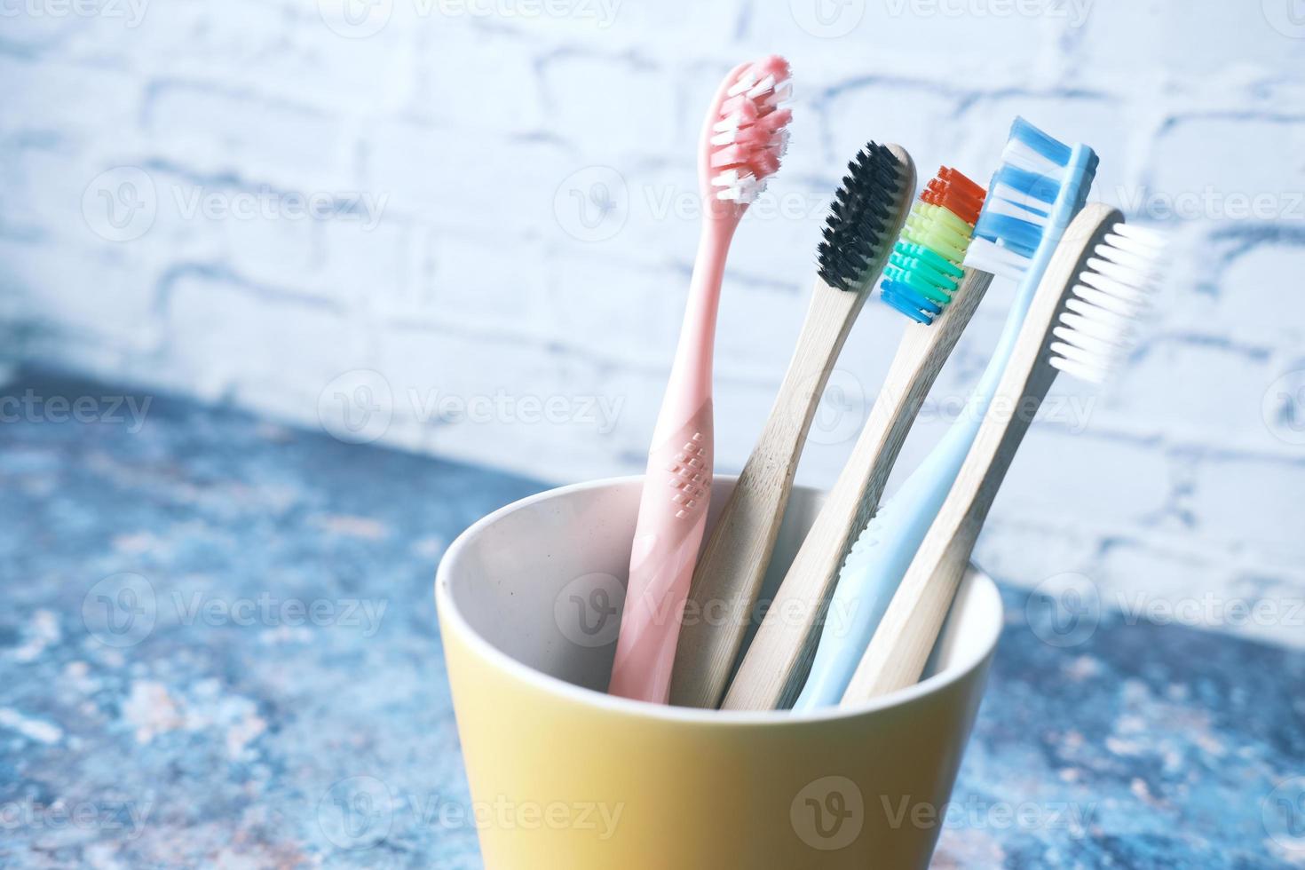 Colorful toothbrushes in white mug against a wall photo