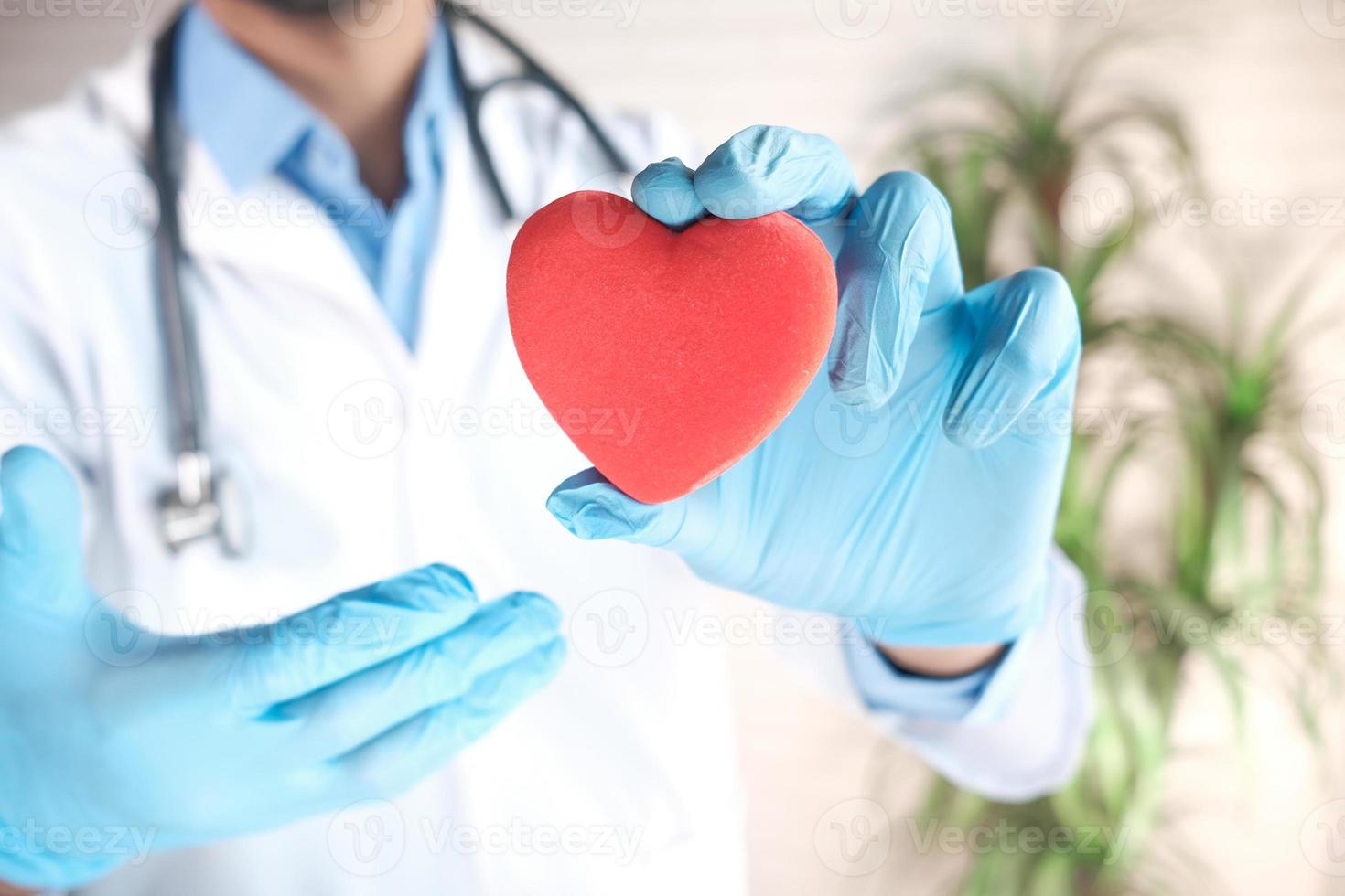 La mano del médico en guantes de látex sosteniendo un corazón rojo de cerca foto